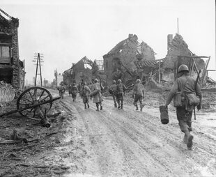 Das infolge der Kämpfe im Westen zerstörte Dorf mit vorbeimarschierenden amerikanischen Infanteristen. Aufgenommen wurde das Foto am 6. Dezember 1944. [Foto U.S. Signal Corps, U.S. National Archives]