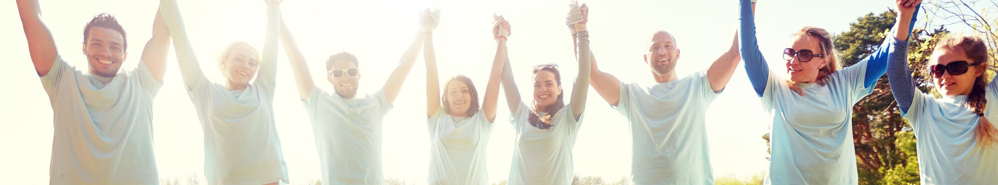 group of happy volunteers holding hands outdoors