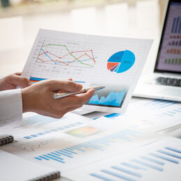 Businessman working at office desk with financial reports and using a touch screen tablet, hands close up, top view