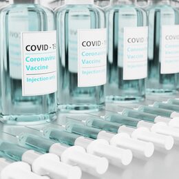 Impf-Flaschen und Spritzen aufgereiht auf einem Tisch