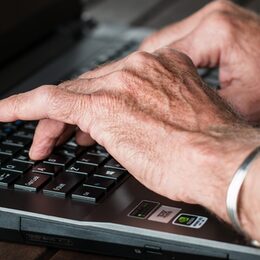 Hände eines älteren Menschen auf einer Laptop-Tastatur