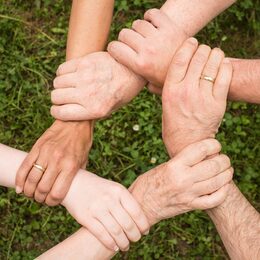 Sechs Hände halten sich im Kreis gegenseitig am Handgelenk fest