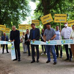 Menschen mit einem Banner in der Hand, das zur Eröffnung des RurUfer-Radweges dient