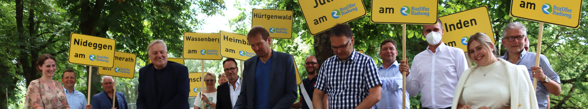 Menschen mit einem Banner in der Hand, das zur Eröffnung des RurUfer-Radweges dient