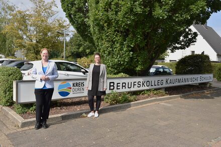 Schulleiterin Christine Stein (links) und die zukünftige Bildungsgangleiterin Britta Münster vor dem Schild der Schule