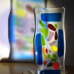 Eine Glasskulptur wirft eine bunte Projektion durch Lichteinfall an die Wand