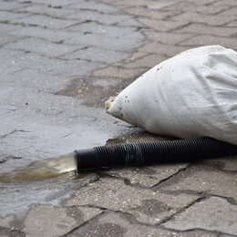 Ein Schlauch, aus dem Wasser läuft. Darauf liegt ein Sandsack.