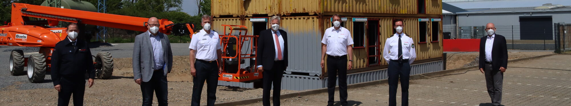 Die Verantwortlichen stehen in Reihe vor dem Containerbau auf dem Gelände