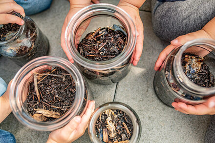 Kinder halten Einmachgläser gefüllt mit Erde und Ästen