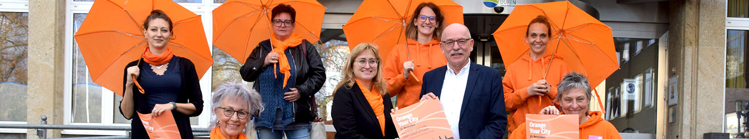 Eine Gruppe Menschen steht mit orangefarbenen Schirmen in den Händen vor dem Kreishaus