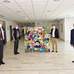 Bunt, vielfältig und voller Leben: Künstler Otmar Alt (hinten links) übergibt das bunte Kunstwerk an die Leiterin der Frauenklinik, Dr. Heike Matz (hinten rechts). Landrat Wolfgang Spelthahn (vorne links) und Leiter Prof. Frank Günter Zehnder freuen sich, dass das Bild vielen Menschen Freude bringen wird. Sie stehen alle mit Abstand um das Bild, der Künstler und die Ärztin halten das Bild in der Mitte.