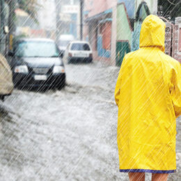 Person mit  Regenjacke steht in überfluteter Straße im Regen