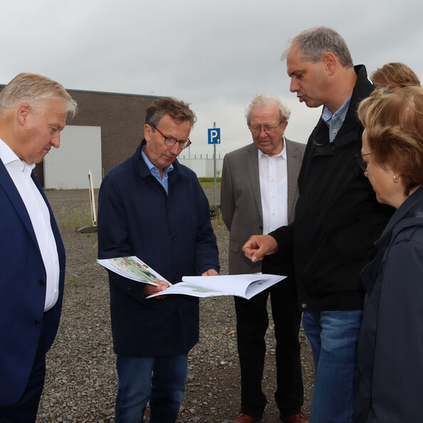 Die Teilnehmer der Sommertour erkunden Morschenich-Neu zu Fuß und schauen auf einen Bauplan.