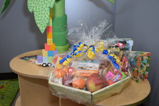 Auf einem mit Spielzeug beladenen Tisch steht der in Folie gepackte Geschenkkorb voller Leckereien.