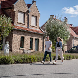 Zwei Personen laufen entlang einer Straße in einem dörflichen Umfeld.