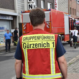 Ein Feuerwehrmann, der von hinten gezeigt wird. Er blickt auf eine Straße, in der Feuerwehrautos stehen.