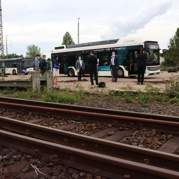 Blick auf den Nordbahnhof. Zusehen sind Schienen im Vordergrund und eine Gruppe von Menschen vor dem Wasserstoff-Bus im Hintergrund.