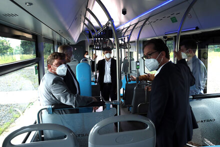 Bürgermeister Axel Fuchs und Geschäftsführer des Brainergy Park, Frank Drewes, stehen mit weiteren Personen im Wasserstoff-Bus.