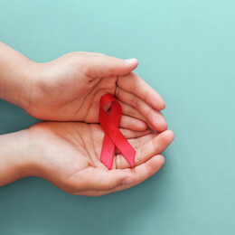 Hands holding red ribbon on blue background, hiv awareness concept, world AIDS day, world hypertension day