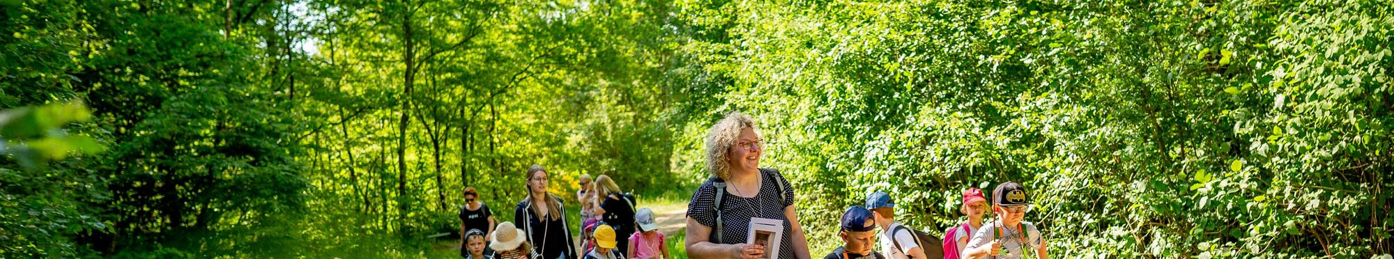 Kinder sind mit Erzieherinnen im Wald unterwegs.