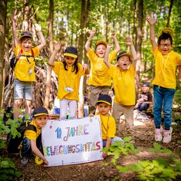 Kinder jubeln im Wald zum Jubiläum "10 Jahre Bewegungskitas"