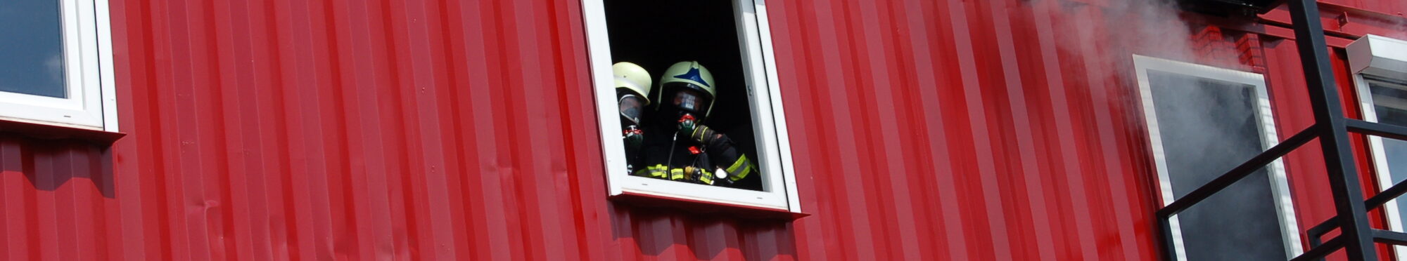 Zwei Feuerwehrleute erscheinen in einem Hausfenster.