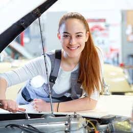 Young female mechanic working on car engine with wrench