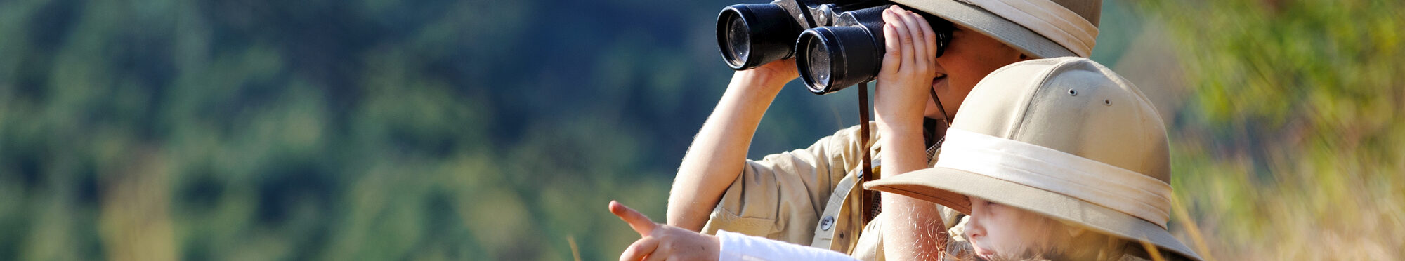 Children brother and sister playing outdoors pretending to be on safari and having fun together with binoculars and hats