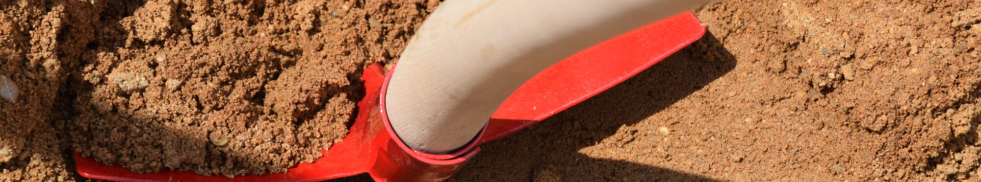 Eine rote Schaufel im Sand.