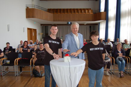 Landrat Wolfgang Spelthahn und zwei Jugendliche wollen den Knopf des Zufallsgenerators drücken.