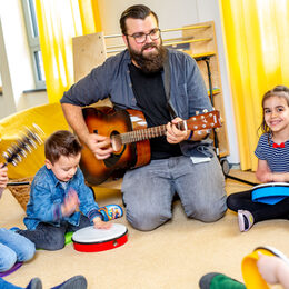 Kinder singen gemeinsam mit einem Erzieher und sitzen im Kreis.