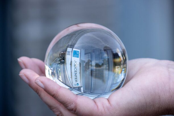 Das Gebäude der job-com spiegelt sich in einer Glaskugel, die auf einer Hand liegt.