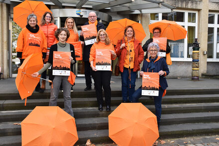 Gruppenbild des Organisationsteams vor dem Kreishaus mit orangenen Regenschirmen.
