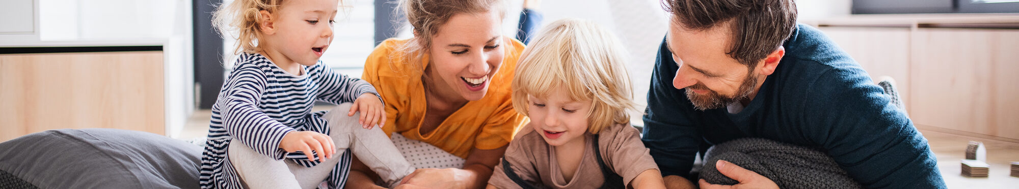 Young family with two small children indoors in bedroom reading a book.