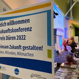 Plakat mit Zukunftskonferenz, im Hintergrund das Panel auf der Bühne