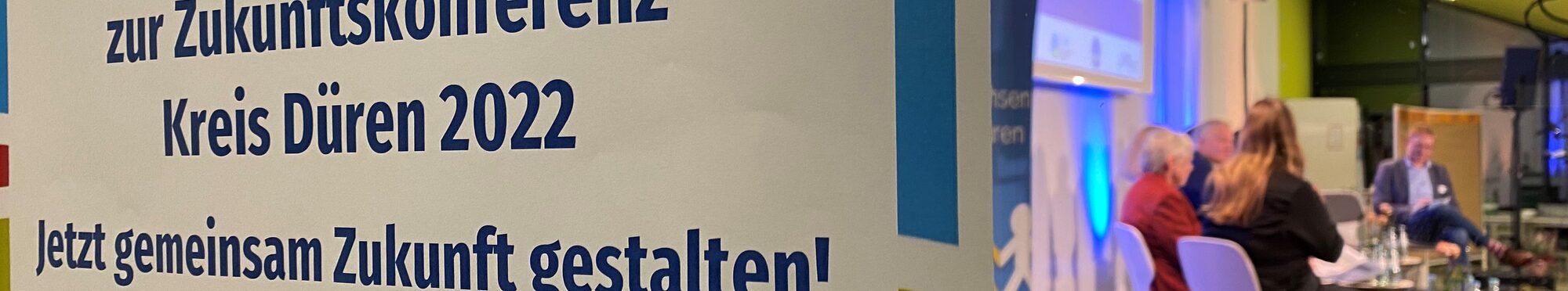 Plakat mit Zukunftskonferenz, im Hintergrund das Panel auf der Bühne