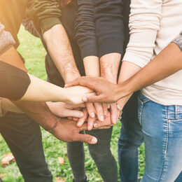 Mehrere Menschen stehen im Halbkreis und legen ihre Hände aufeinander.