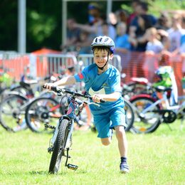 Ein Junge mit hält sein Fahrrad fest und läuft daneben.