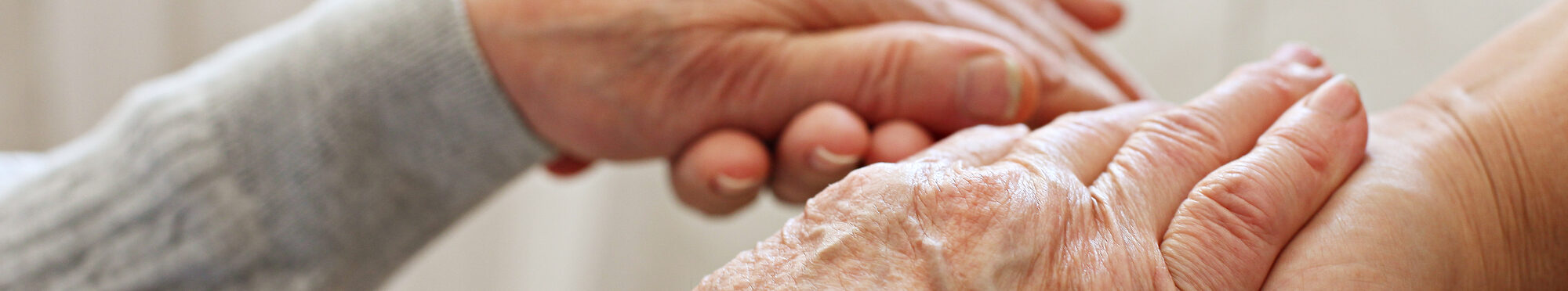 Mature female in elderly care facility gets help from hospital personnel nurse. Senior woman w/ aged wrinkled skin & care giver, hands close up. Grand mother everyday life. Background, copy space.