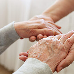 Mature female in elderly care facility gets help from hospital personnel nurse. Senior woman w/ aged wrinkled skin & care giver, hands close up. Grand mother everyday life. Background, copy space.