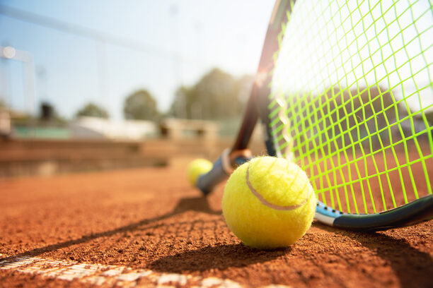 Tennisball und -schläger liegen auf einem Asche-Tennisplatz