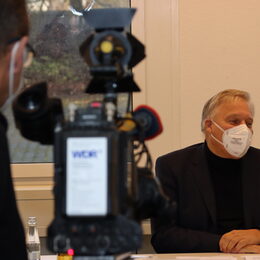 Landrat Wolfgang Spelthahn sitzend am Tisch, während ein Kamerateam ihn filmt.