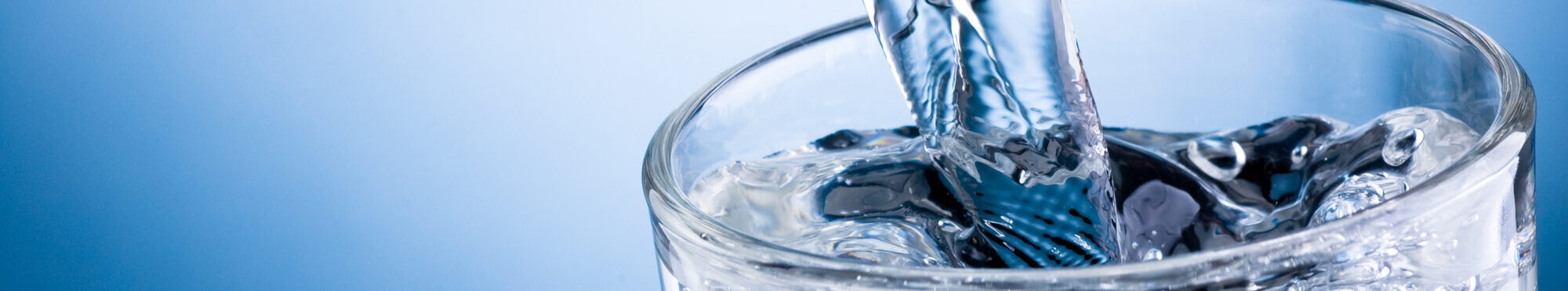 Pouring water into glass on blue background