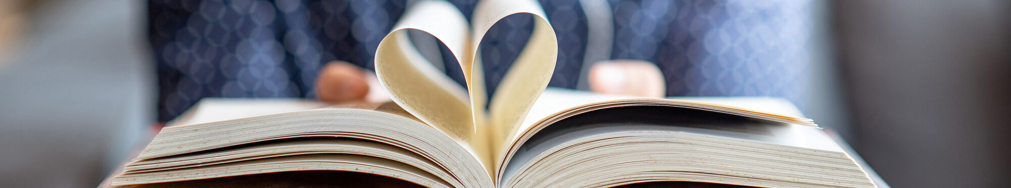 Book lover or love reading concepts. Male hand holding book with heart shape page folded.