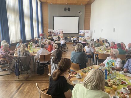 Viele Menschen sitzen gemeinsam in einem Sitzungssaal des Kreises Düren und frühstücken.