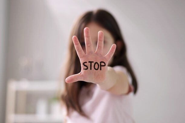 Ein Mädchen streckt zur Abwehr die Hand nach vorne. Darauf geschrieben steht das Wort "stop".