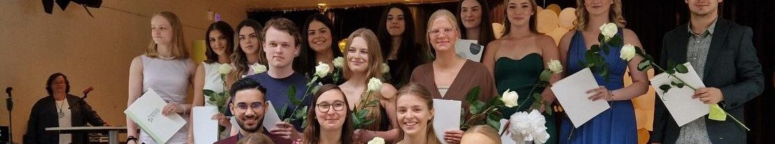 Eine Gruppe junger Menschen, die ihren Abschluss gemacht haben, steht auf einer Bühne.