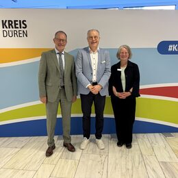 Das Bild zeigt zwei Männer und eine Frau vor einer Stellwand des Kreises Düren
