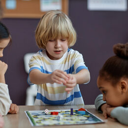 Kinder sitzen gemeinsam vor einem Brettspiel und spielen.