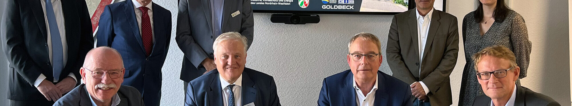 Das Bild zeigt zehn Personen bei der Vertragsunterzeichnung an einem Tisch
